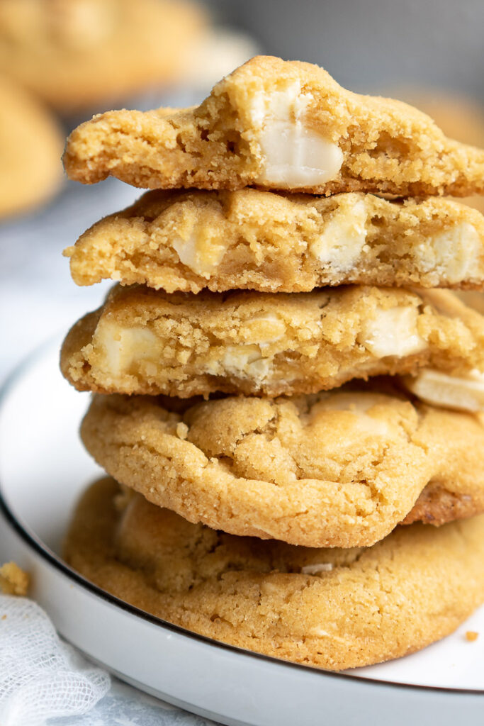two whole white chocolate macadamia cookies and 3 halves in a stack on a white plate