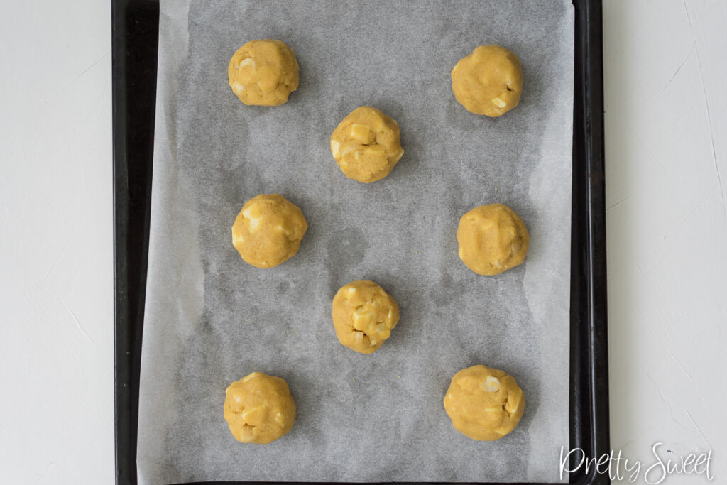 ball of cookie dough with white chocolate and macadamia on a black baking tray lined with parchment paper