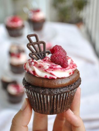 Raspberry chocolate cupcake with cream cheese frosting topped with raspberries up close in hand