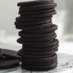 Round black cocoa shortbread cookies in a tall stack
