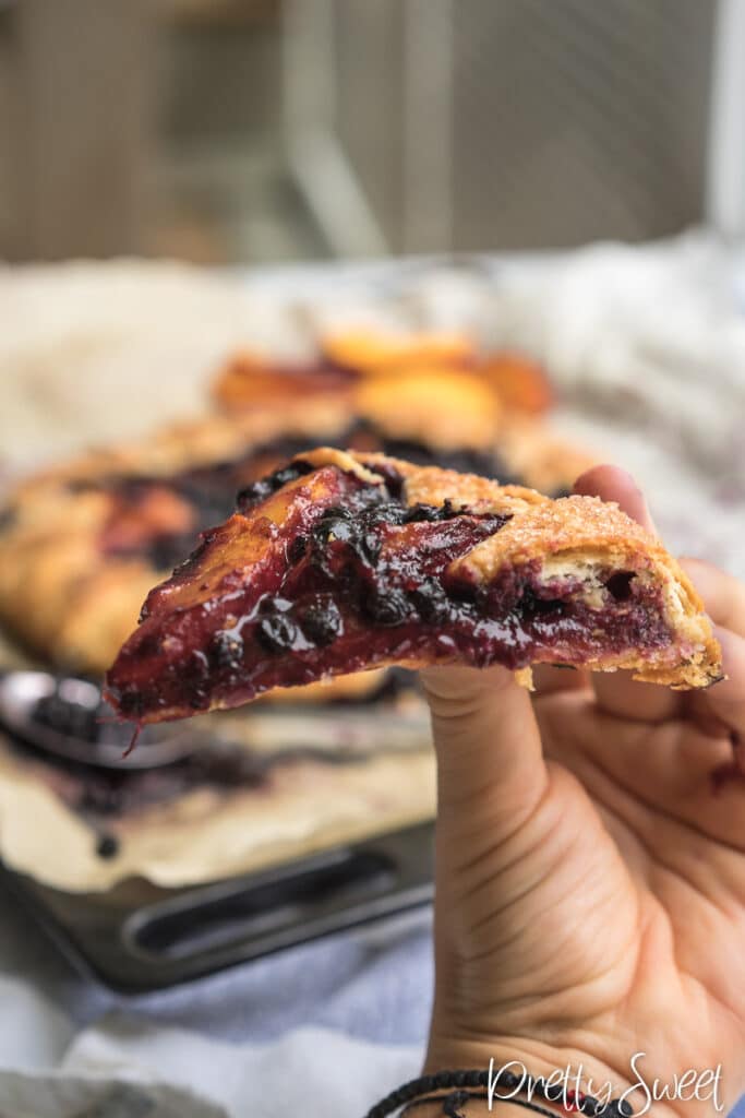 A piece of a peach blueberry galette held in hand