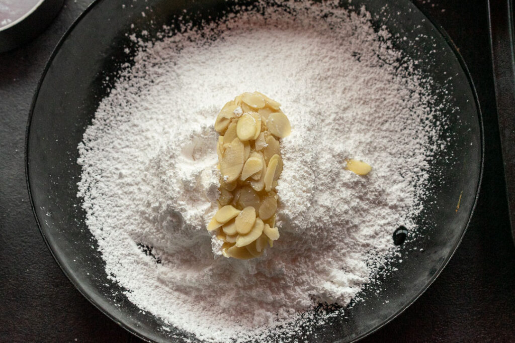 oval shaped amaretti cookie dough on powdered sugar in a plate