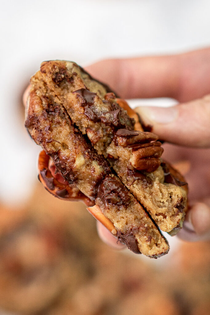 a chewy pecan cookie halved and held in hand