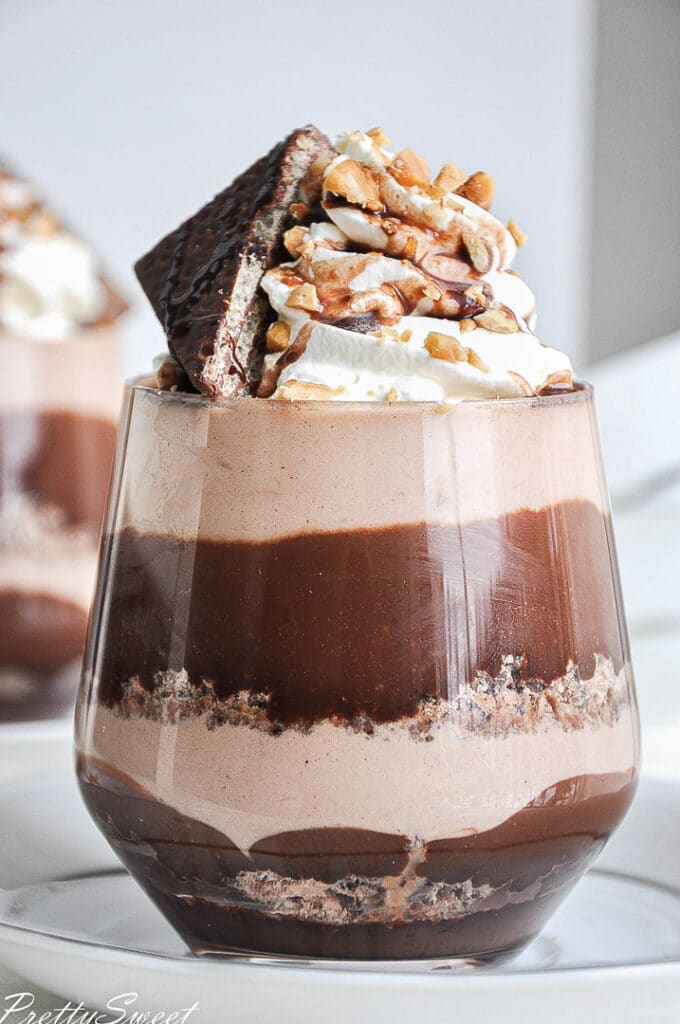 a glass full of chocolate and hazelnut mousse layers and whipped cream on top with hazelnut pieces and a chocolate wafer