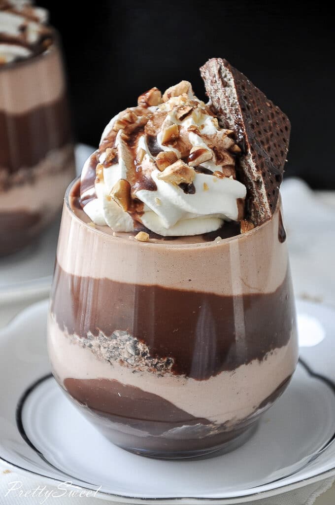 a layered chocolate hazelnut dessert in a glass with whipped cream on topand a chocolate wafer