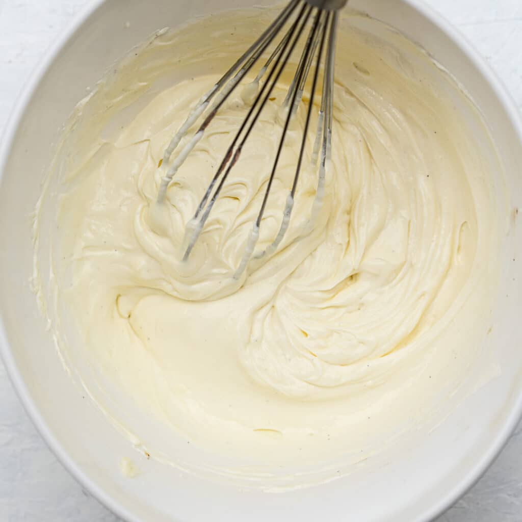 cheesecake batter in a white bowl with a whisk