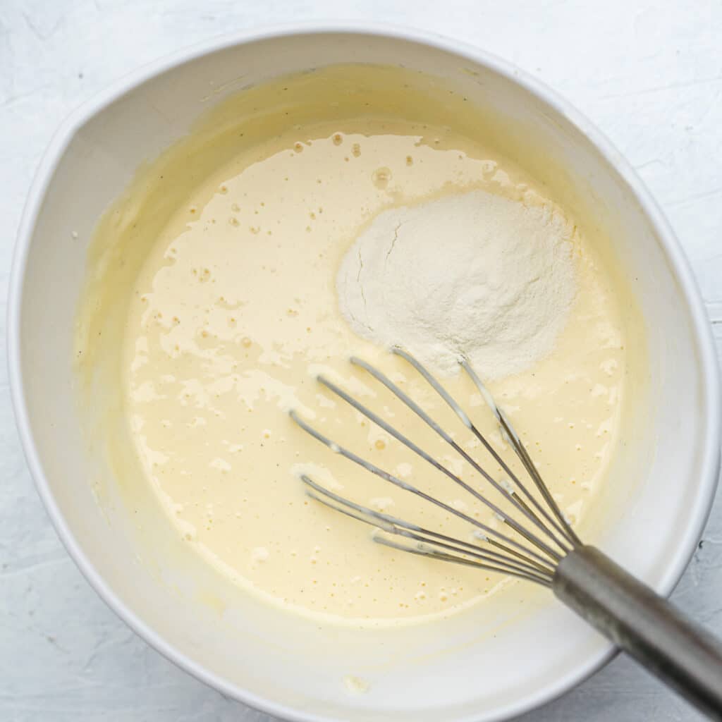 added flour to the cheesecake batter in a white bowl with a whisk