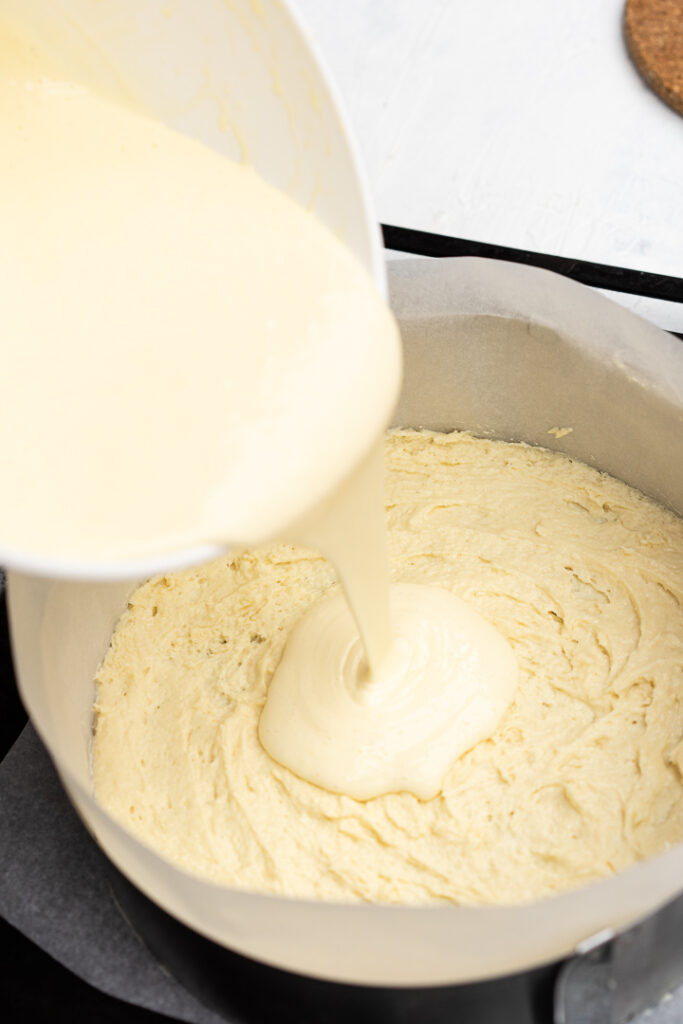 pouring cheesecake filling on the cinnamon roll batter in the pan